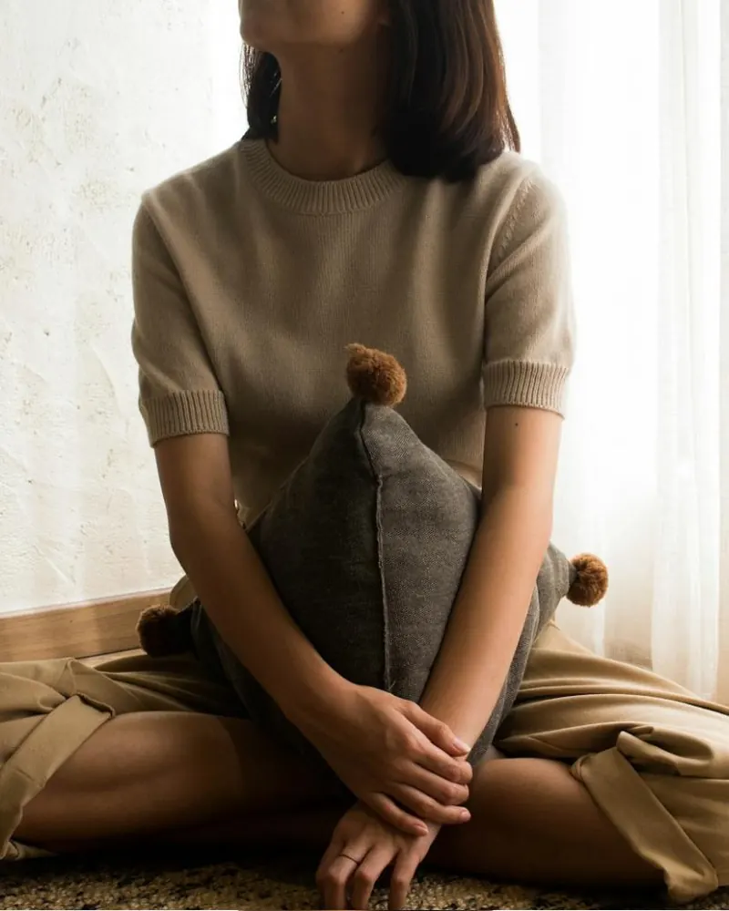 A person sitting cross-legged on a rug by a sunlit window, holding a cushion
