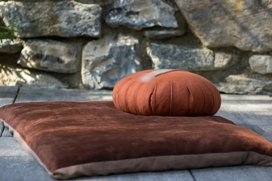 A round cushion resting on a flat floor cushion in front of a stone wall