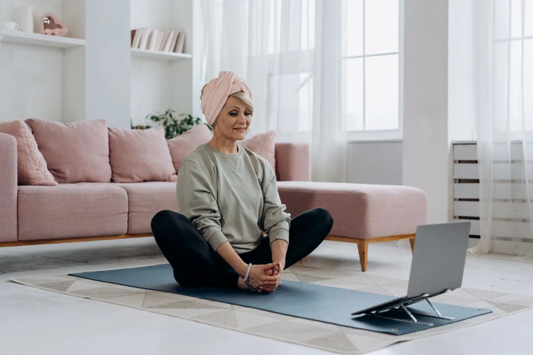 Person meditating at home with a laptop nearby