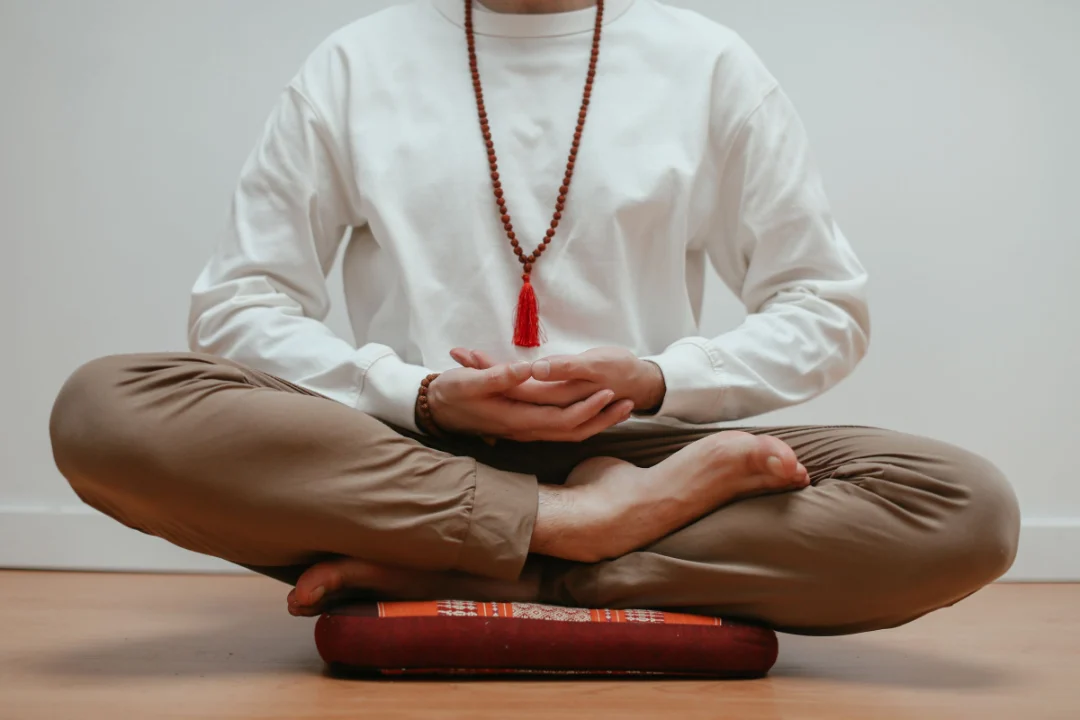 Person seated cross-legged on a firm floor cushion with hands resting in the lap